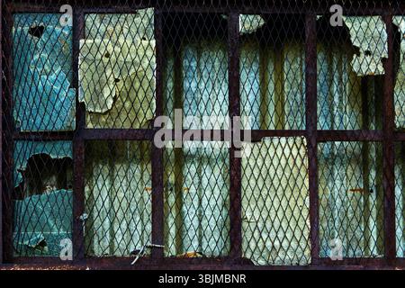 The weathered window features damaged glass and rusty metal bars, showing signs of decay and neglect in an abandoned structure. Stock Photo