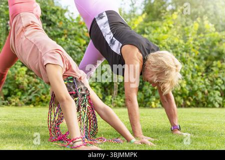Fexible girl and mature woman together in sportswear raising leg and bending forward at the garden.  Horizontally. Stock Photo