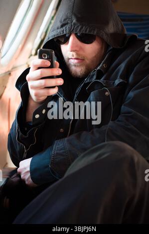 Hooded man looking at his cellular phone in an old airplane Stock Photo