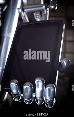 Robot hand holding tablet pc against dark background Stock Photo