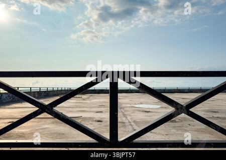 Urban metal fence with geometric pattern on concrete surface, captured in sunlight with empty space and sky. No people. Stock Photo