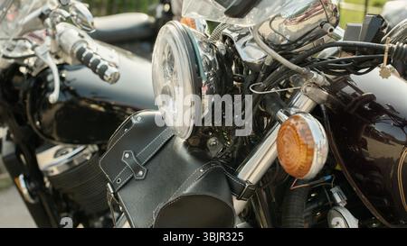 Vintage motorcycle close-up featuring a polished chrome headlight, amber turn signal, exposed wiring, and a black leather fork bag with white stitchin Stock Photo