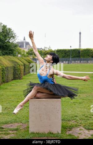 Ballet dancer stretching arms in elegant pose on garden pedestal Stock Photo