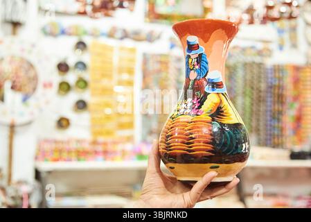 Female hand holding a handcrafted ceramic vase painted with a colorful traditional scene, in Raquira, Colombia, town known for its handicrafts and pot Stock Photo