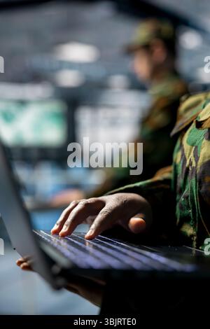 Close up of military server room worker typing on laptop, overseeing firewall configurations. Army information technology specialist in data center deploying software updates in secure facility Stock Photo