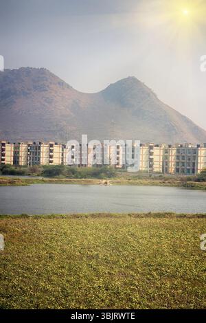 New village under construction in India on backdrop of mountains (foothill, foothill belt, submountain region) and railroad, apartment buildings. Evid Stock Photo
