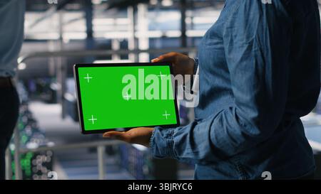 Close up of IT experts using chroma key device to analyze neural networks outputs. Data center admin uses green screen tablet next to colleague reviewing AI visualization in blurry background Stock Photo