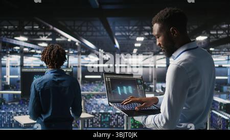 Server hub coworkers visualizing large language model architecture using notebook. Data center technicians on industrial platform collaborating on neural network software tasks using laptop Stock Photo