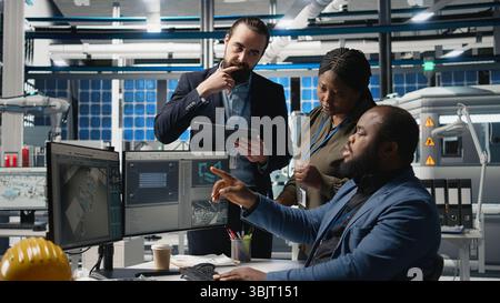 Multiethnic master engineers doing teamwork on high tech production line for solar panels manufacturing activity, combining technical insight and collaboration for green energy. Camera A. Stock Photo