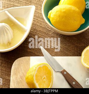 Sliced lemons, knife, and citrus juicer on rustic surface Stock Photo