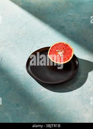 Sliced grapefruit on black plate with blue textured surface Stock Photo
