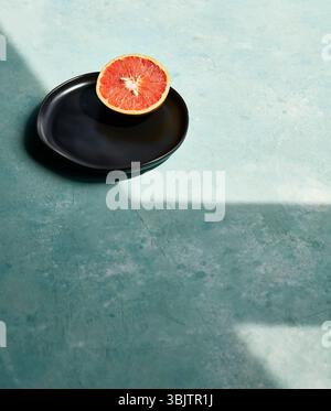 Sliced grapefruit on black plate with blue textured surface Stock Photo