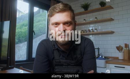 Bearded man wearing a black tactical vest looks directly at the camera with a calm, confident expression in a modern indoor setting. Stock Photo