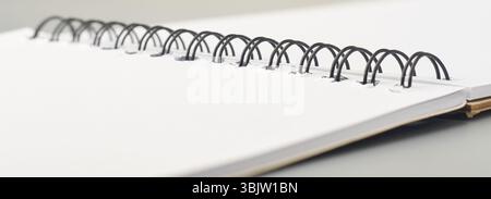 close-up of black metal spiral binding of open notebook or sketchpad on gray surface, side view taken in soft focus with copy space Stock Photo
