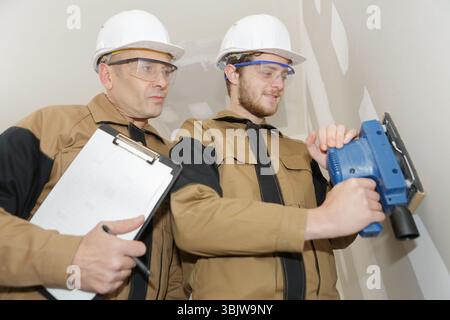 apprentice using sander on wall under supervision Stock Photo