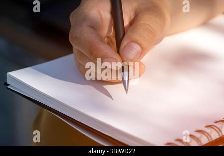 A male hand holds a pen and writes in a sketchbook, notepad closeup. Stock Photo