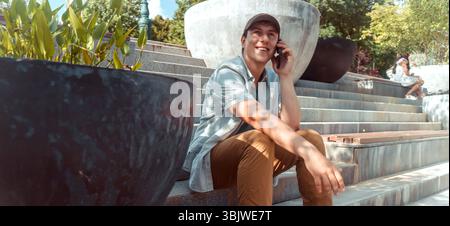 A young happy man talks, communicates on a smart phone outdoors. Stock Photo