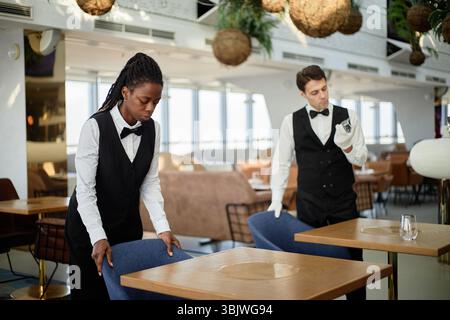 Young Adult Black Woman and Caucasian Man Arranging Chairs in Restaurant Stock Photo