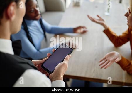 Young Caucasian Man Using Smartphone While Talking with Diverse Clients Stock Photo