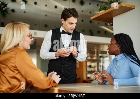 Young Adult Caucasian Waiter Taking Order from Diverse Women Stock Photo