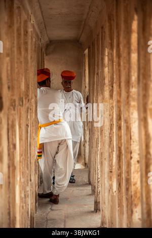 Two indian men wearing traditional white clothes and colorful turbans are talking in a narrow corridor inside City Palace, Udaipur, Rajasthan, India, Stock Photo