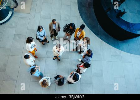 Overhead view of a diverse group of professionals standing in a circle during a corporate meeting. The setting exudes a sense of collaboration, teamwo Stock Photo