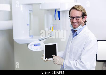 Dental professional pointing at tablet screen while standing next to X-ray machine in clinic room Stock Photo