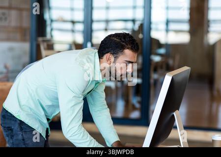 Office worker leaning over desk at monitor in office, focusing on code with coffee cup nearby Stock Photo