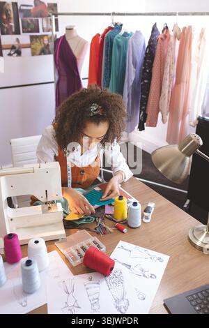 Fabric swatches lying beside sewing machine on wooden desk in fashion studio with thread spools Stock Photo