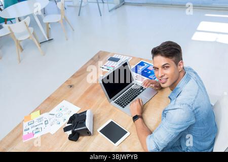 Mid adult man wearing denim shirt working on laptop with VR headset in office, copy space Stock Photo