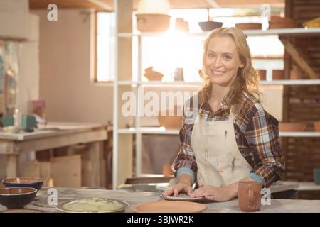 Sunlight streaming through window casting light on clay and pottery tools on bench, pots on shelves Stock Photo