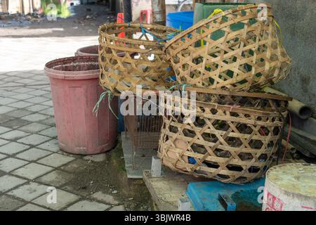 Pile of baskets and a red trash can sit on a brick sidewalk. The baskets are made of wood and are arranged in a stack. The trash can is placed in the Stock Photo
