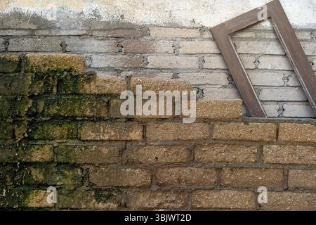 Brick wall with a window frame on top of it. The window frame is missing a pane Stock Photo