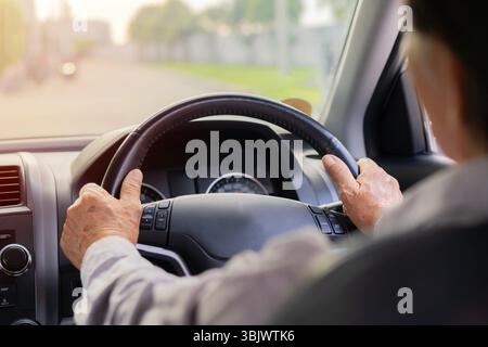 Senior Adult's Hand on the Steering Wheel. Back view shot, selective focus of older man's hands. Lifestyle of elderly concept. Stock Photo