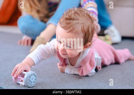 Happy baby girl lying on carpet reaching for toy while playing at home Stock Photo