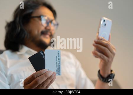 Bearded handsome man wearing eyeglasses using mobile phone for online shopping. Selective focus on credit card mock up. Payment online concept. Stock Photo