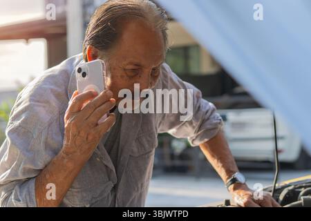 Mature man trying to fix his car when talking on phone with mechanic. A car owner is calling a car repair shop to check condition of car. Stock Photo
