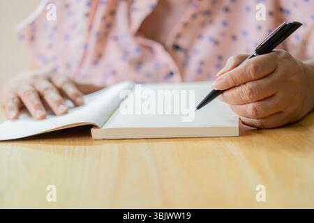 Hands of unrecognizable senior woman writing on notebook with pen in livingroom at home. Retirement writing concept. Stock Photo