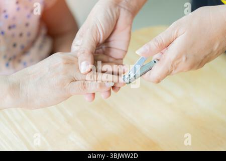 Close-up of the fingernails of two unrecognizable women. Manicure cutting on the older woman's nails on the table at home. Helping support to elder pe Stock Photo