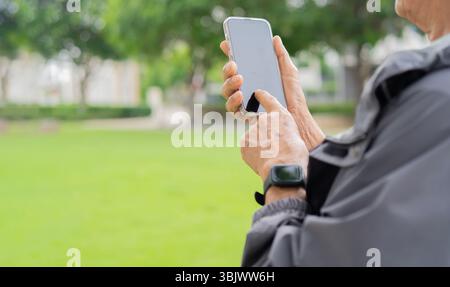 Cropped view of senior man using mobile phone in a field at sunset. Senior man using smartphone outdoors. Copy space, selective focus. Stock Photo