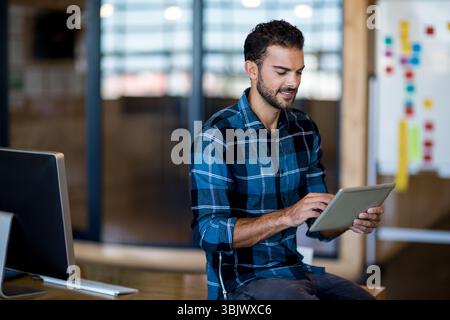 Tablet resting on wooden desk in modern office, with computer monitor whiteboard and sticky notes Stock Photo