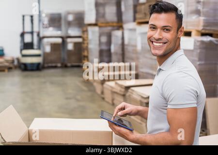 Male worker wearing light gray polo shirt scanning inventory on tablet beside open box in warehouse Stock Photo