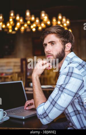 Man using laptop drinking coffee at wooden table in cafe with chandelier lights, copy space Stock Photo