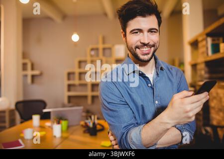 Wooden desk displaying mugs, pencils, sticky notes, laptop beneath warm pendant lights in office Stock Photo