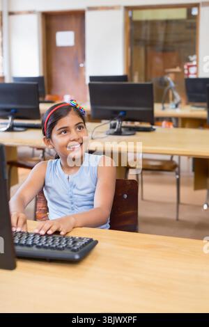 Indian girl child typing on keyboard at school computer lab with desktop monitor and wooden desk Stock Photo