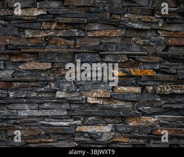 Detailed background texture of a dark stone wall made from stacked slate tiles. The natural rock facade features shades of grey, black. Backdrop Stock Photo