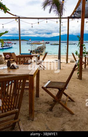 Gili, Lombok, Indonesia - Jan 3, 2025: Beach with a wooden table and chairs. The chairs are empty. The table is covered with a tablecloth Stock Photo