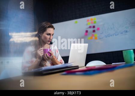 Woman holding purple mug and typing on laptop at modern office wooden table with sticky notes Stock Photo