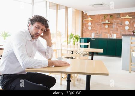 Man sitting at wooden cafe table resting head on hand holding coffee cup, copy space Stock Photo