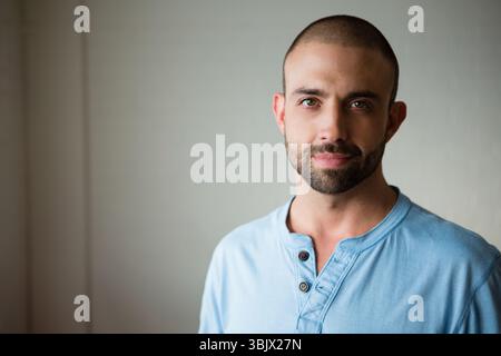 Man standing against smooth painted wall in studio wearing light blue henley shirt, copy space Stock Photo
